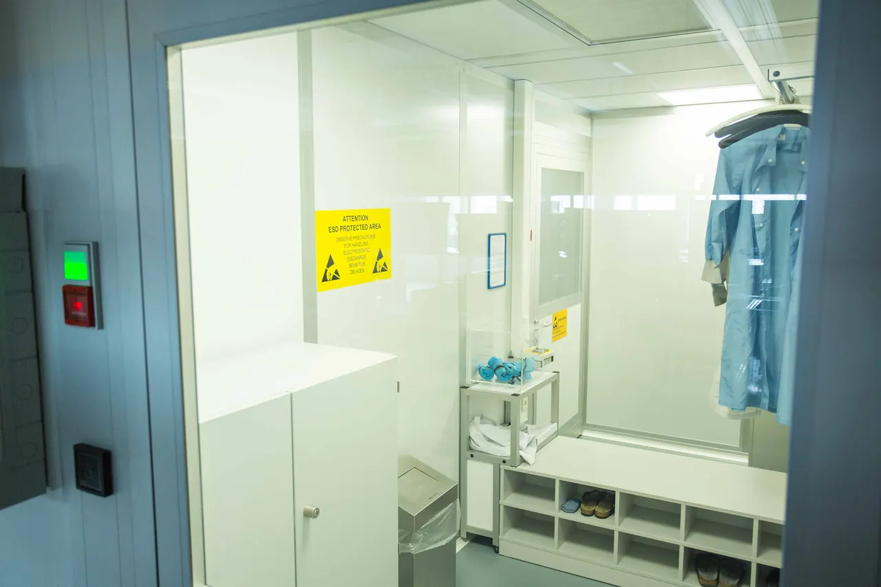 Blick in die Schleuse vor der ESD-Schutzzone mit Warnschild, blauen ESD-Kitteln am Haken und Schuhregal